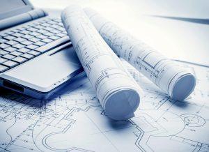 Rolled engineering drawings beside a laptop on a desk