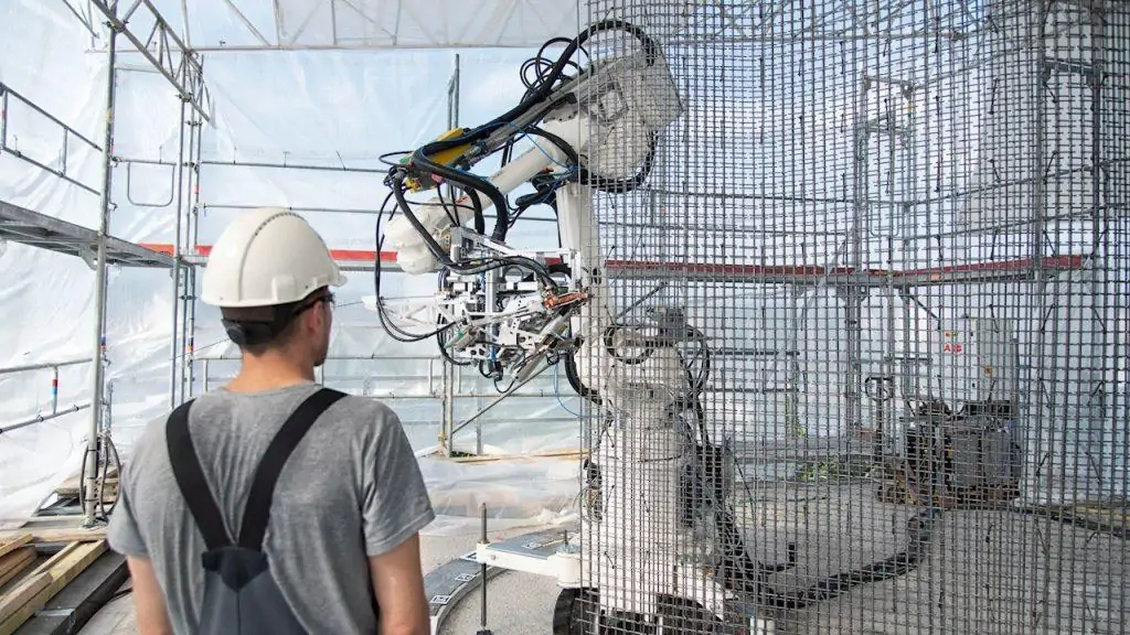 Worker observing a robotic arm operating beside a reinforcement mesh structure